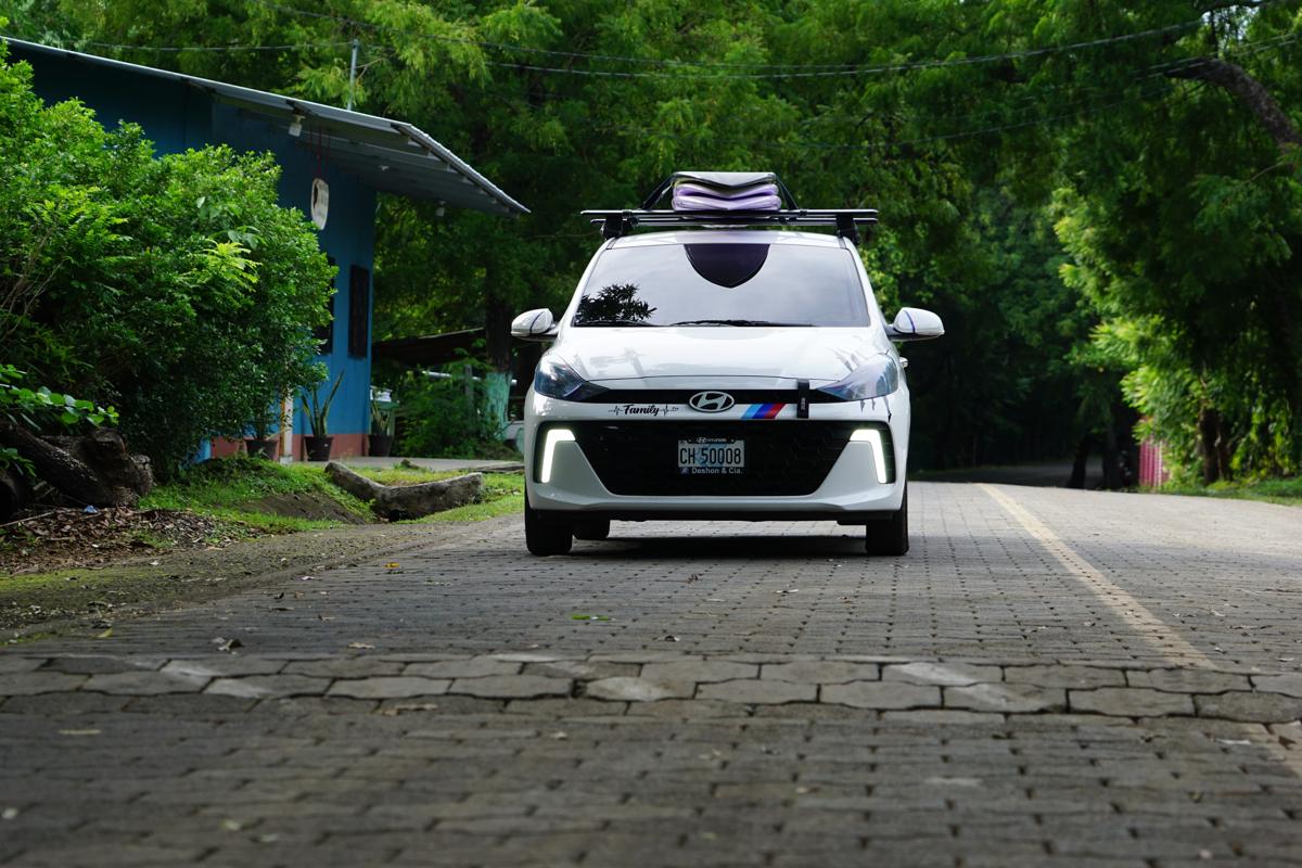 White Panda on Wheels taxi with surfboards on the roof rack, on a cobblestone road under trees